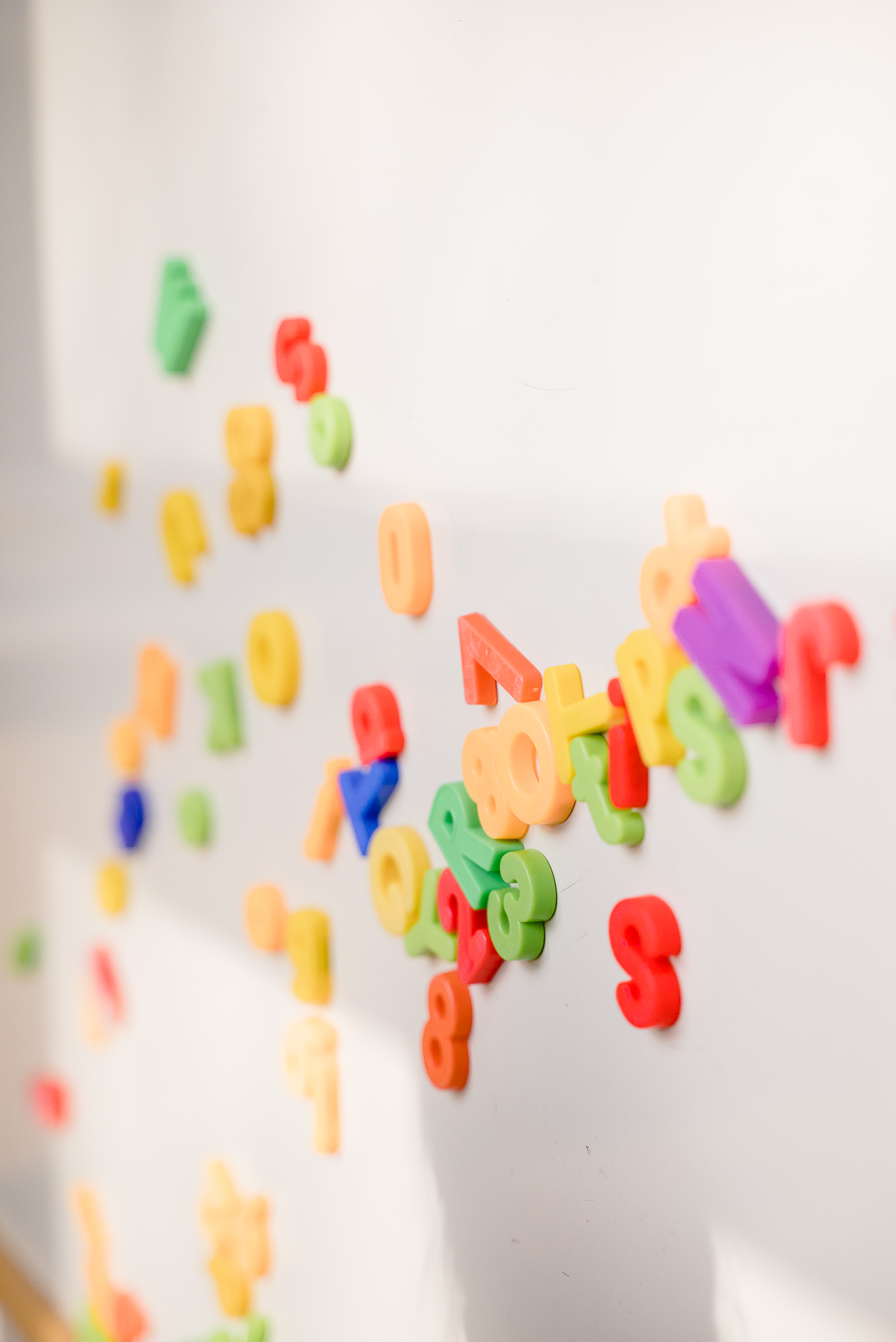 Bunte Magnetbuchstaben und -zahlen auf einer weißen Oberfläche, verstreut angeordnet.