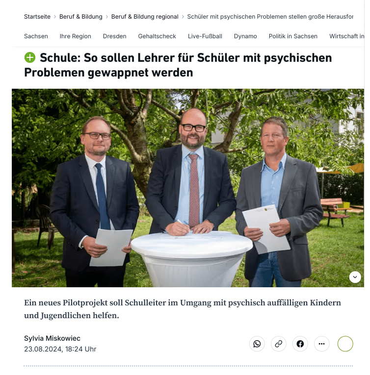 Gruppenfoto von drei Männern im Freien, die an einem runden Tisch stehen und Dokumente halten. Sie diskutieren offenbar ein neues Pilotprojekt zur Unterstützung von Schülern mit psychischen Problemen.